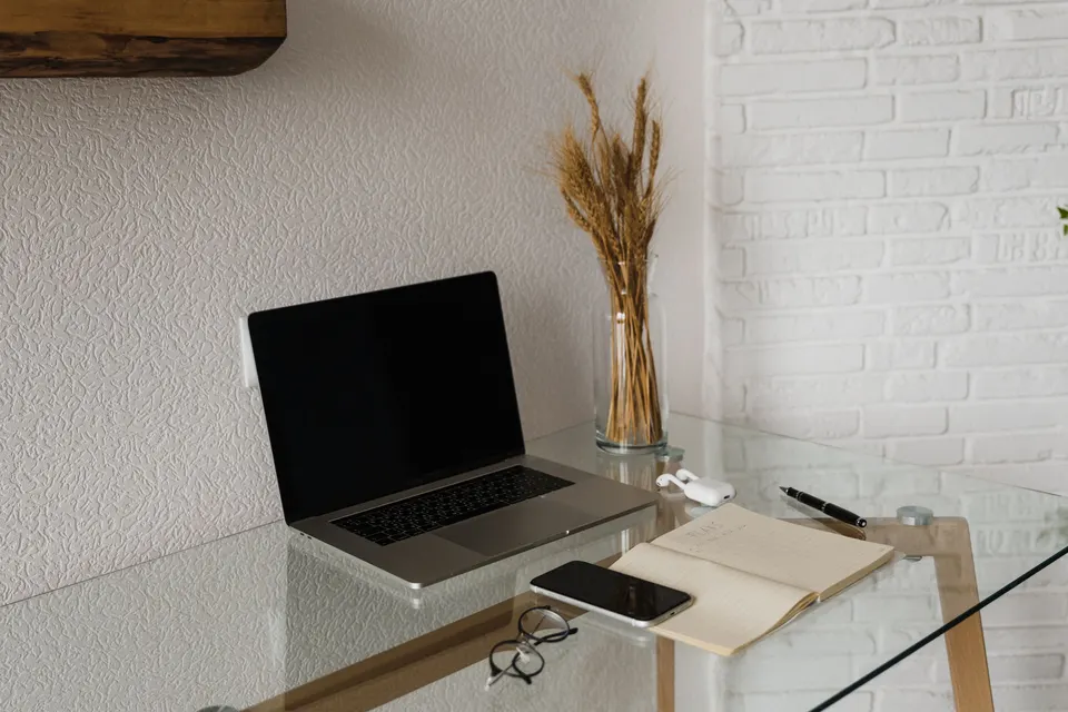 A laptop, phone and open notebook on a glass desk