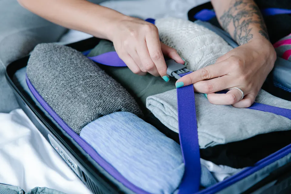 Hands fastening a strap over clothes packed in an open suitcase